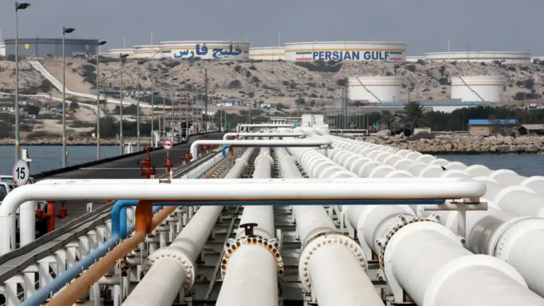 EPA View of Kharg Island oil terminal, showing a row of pipes stretching into the distance towards a raised area of ground where several silos sit, one of them has the words "Persian Gulf" on its side.