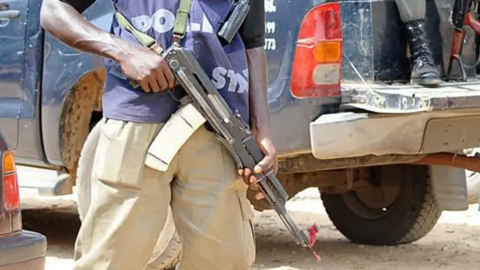 AFP via Getty Images Armed police officer stands beside the back of patrol trucks, holding a rifle in Jos, Plateau State.