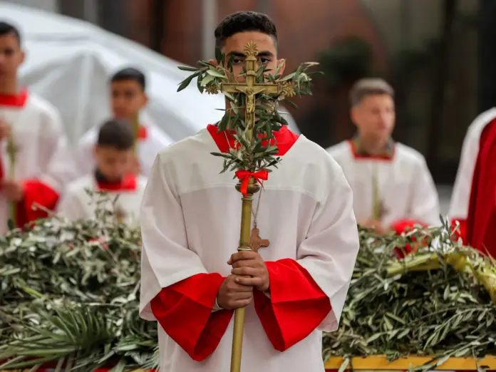 TOPSHOT - An altar server stands with a crucifix adorned with olive branches during the Palm Sunday service at the Roman Catholic Church of the Holy Family in Gaza City on March 29, 2026.