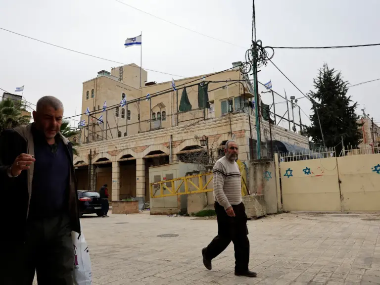 Palestinians walk in front of an Israeli settlement in Hebron
