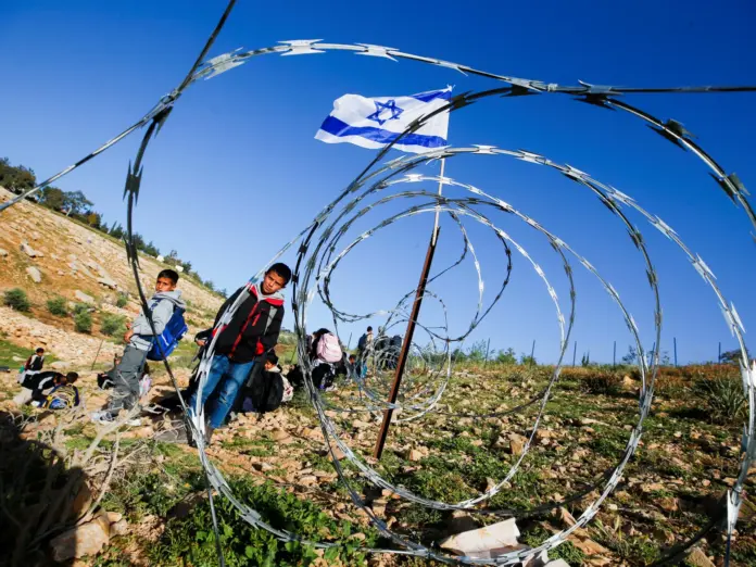 Palestinian students gather near a fence erected by Israeli settlers