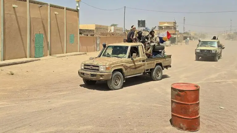 AFP via Getty Images FLA fighters sitting in a pickup truck on a sandy road, with another in the distance behind them. to the left are buildings lining the road. In the front right, there is an orange metal barrel