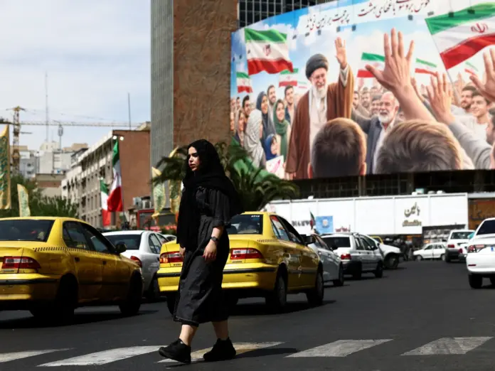 A woman walks past a billboard featuring an image of the late supreme leader of Iran, Ayatollah Ali Khamenei, on a building.