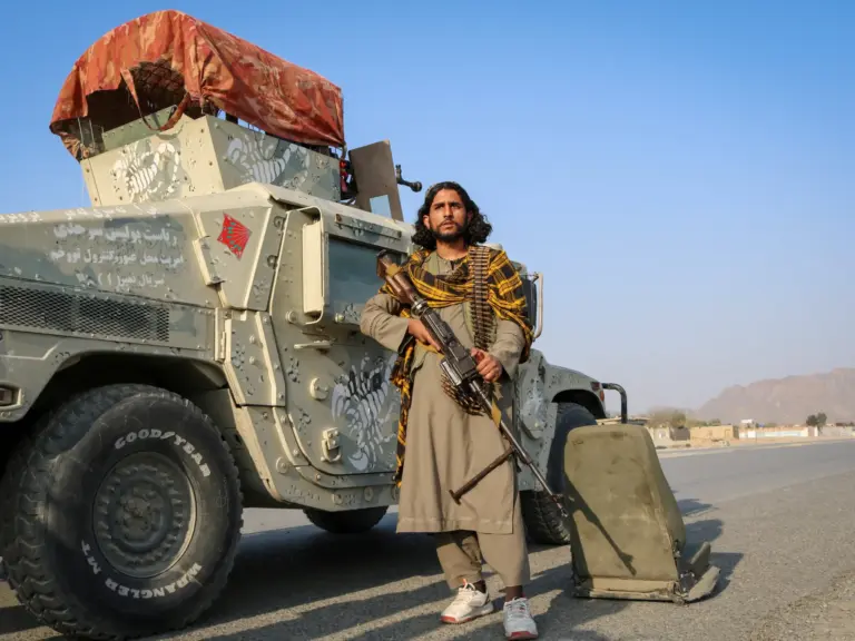 A Taliban soldier holds his gun as he stands next to a Humvee.