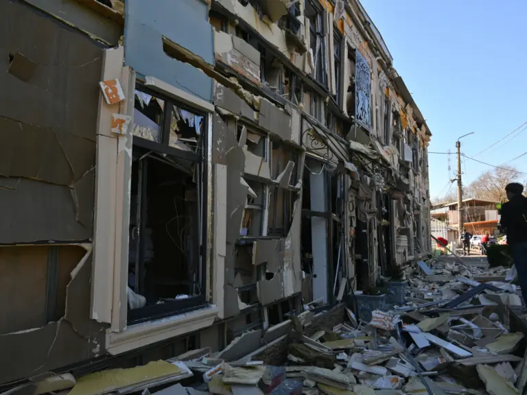A person walks near houses damaged by attacks.
