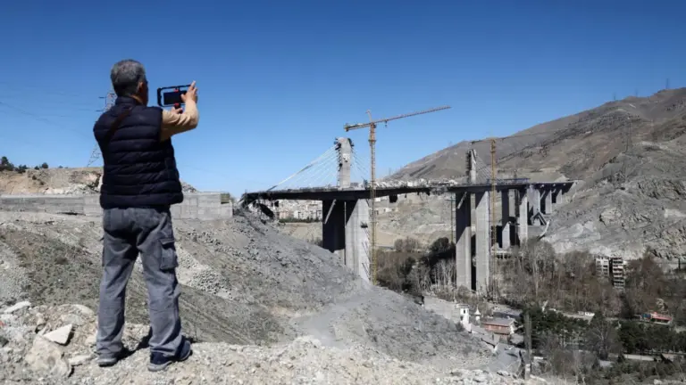 WANA via REUTERS A man uses his phone to photograph the remains of the B1 bridge following a US air strike, in Karaj, northern Iran (3 April 2026)