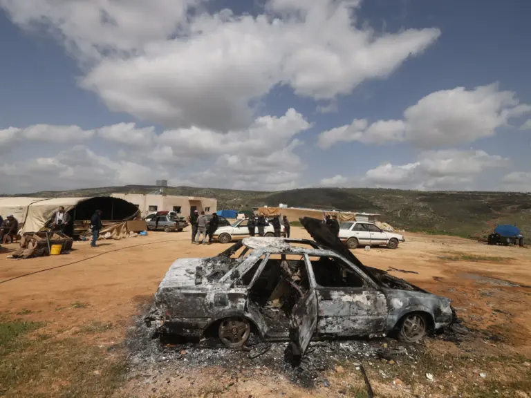 Palestinians stand near a vehicle that was destroyed.