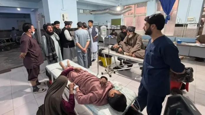 HANDOUT A young male is seen lying down on a stretcher in a hospital ward, hooked up to a drip, as a woman kneels by his side and holds his hand. A man in scrubs is seen stood next to the stretcher looking on at a group on men gathered at the end of the stretcher, while another person can be seen lying on a stretcher in the background