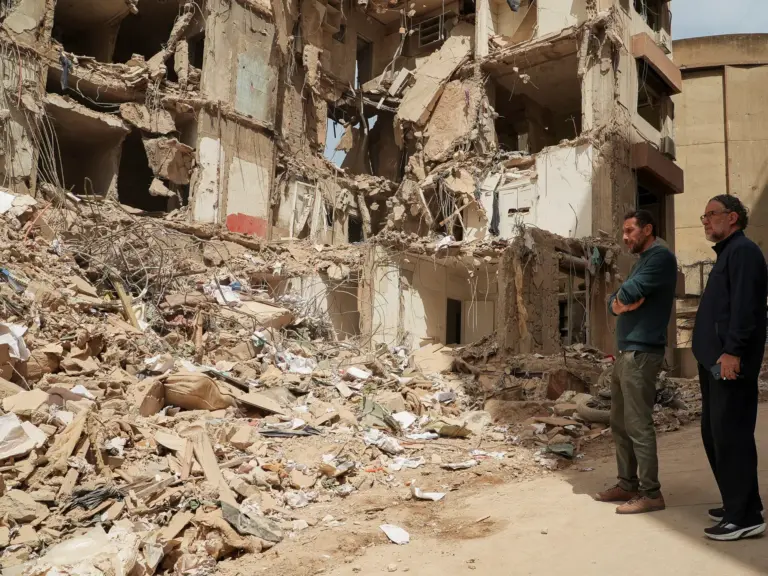 Two men stand at the site of a destroyed apartment building.