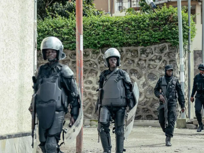 Members of the M23 wearing riot gear stand guard in a street.