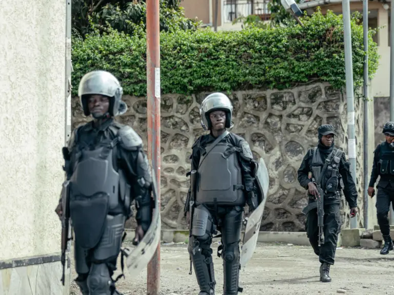 Members of the M23 wearing riot gear stand guard in a street.